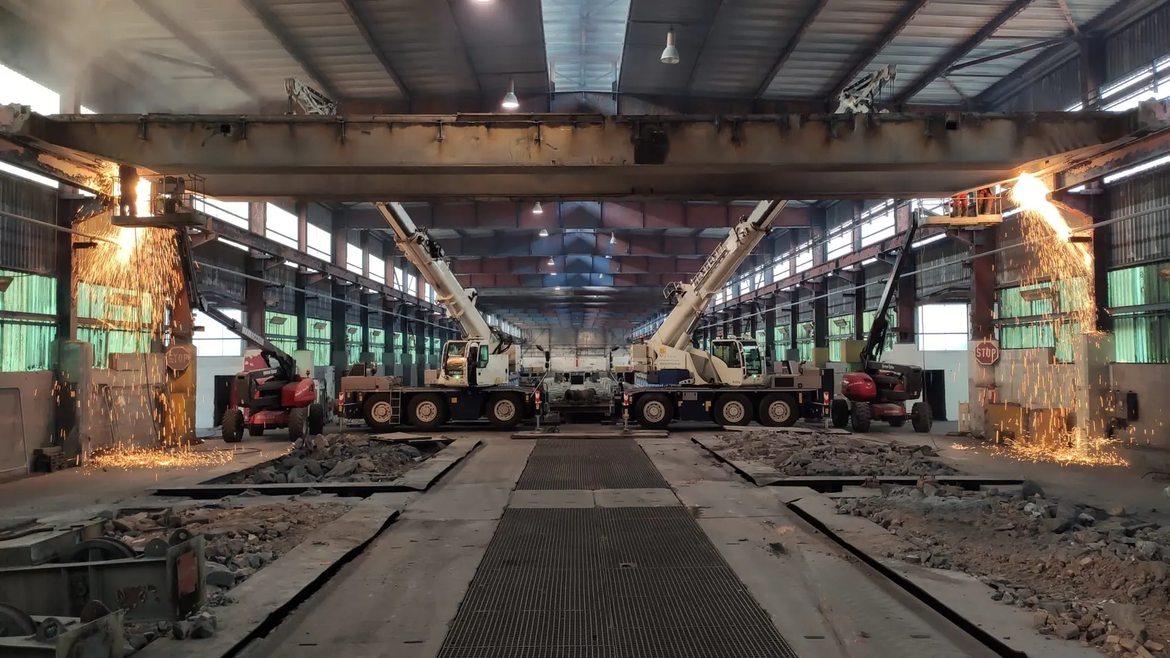 Rückbau in einer Industriehalle: zwei Mobilkrane unter einem Kranbahnträger, Brennschneidarbeiten mit Funkenflug